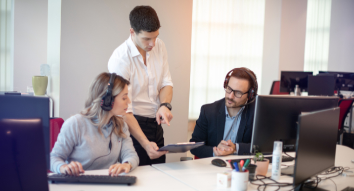 Eine Frau und zwei Männer im Gespräch in einer Arbeitssituation, bei der einer der Männer den anderen beiden etwas erklärt.