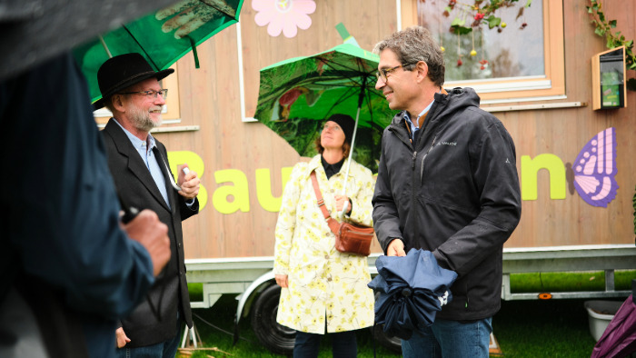 Staatssektretär Andre Baumann steht mit Regenschirm vor dem Natourbauwagen im Rahmen der KLIMA.LÄND.TAGE 2024