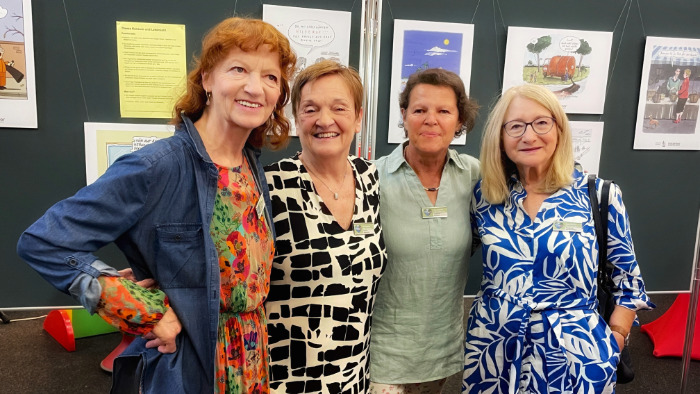 Vier Mitglieder der Omas for Future stehen vor einer Wand mit Karikaturen.