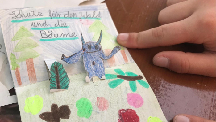 Selbstgemachte Pop-Up Karte eines Kindes mit dem Klimamonster im Wald, das mehr "Schutz für den Wald und die Bäume" fordert.