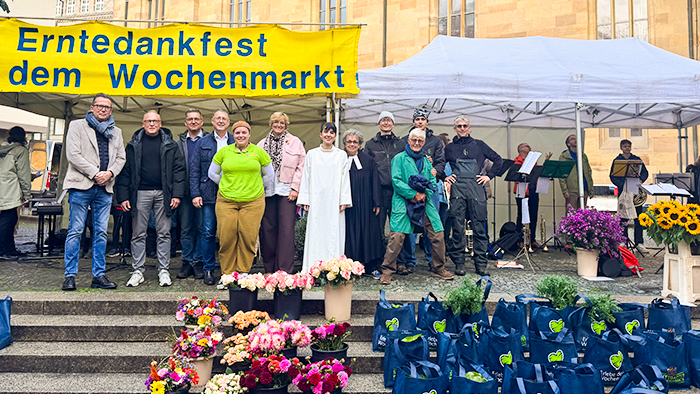 Menschen stehen vor einem Pavillon des Erntedankfestes der Stuttgart Märkte GmbH mit Blumen und Taschen.