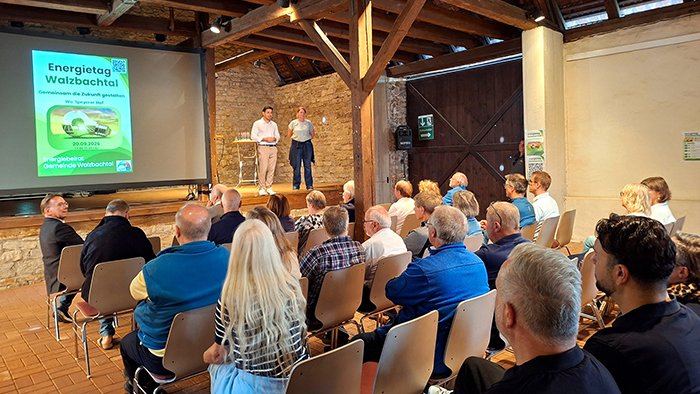 Bürgermeister Özcan steht mit einer weiteren Person auf der Bühne vor der Leinwand „Energietag Walzbachtal“