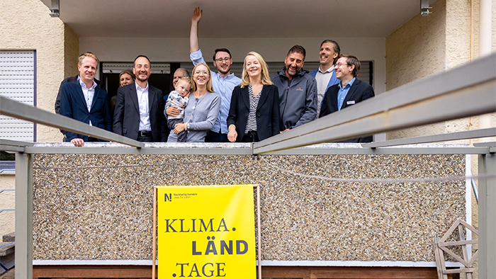 Alle stehen mit Umweltministerin Thekla Walker auf dem Balkon des zu sanierenden Hauses und lächeln in die Kamera.